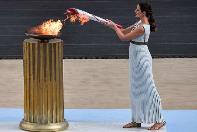 Snímek: Řecká herečka Xanthi Georgiou v roli velekněžky zapaluje pochodeň z plamene v kotli během ceremoniálu předávání olympijského ohně na Panathénském stadionu v Aténách, Řecko; 19. října 2021 / CPF
