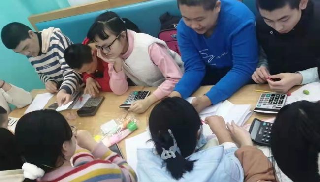 Snímek: Dobrovolníci z Univerzity Guanghua ve městě Changchun učí osoby s mentálním postižením, jak používat kalkulačku v restauraci Wang Chunzhi; 10. prosince 2021. /Lyu Ankang