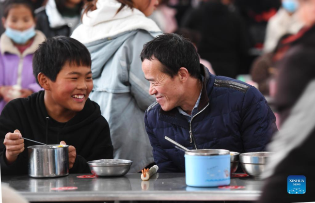 Ο Λου Γουεντζιάν (δεξιά) τρώει μαζί με έναν μαθητή σε σχολείο στο Σανγκτσιό, στην επαρχία Χενάν της κεντρικής Κίνας, 2 Δεκεμβρίου 2021. (Xinhua/Zhang Haoran)