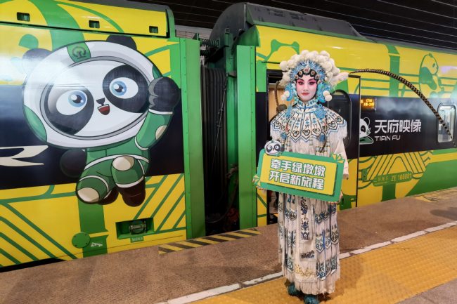 Υπάλληλος του σιδηροδρομικού με κοστούμι όπερας του Σιτσουάν χαιρετά επιβάτες μπροστά σε ένα τρένο σφαίρας ζωγραφισμένο με εικόνες τοπικών πολιτιστικών στοιχείων στον ανατολικό σιδηροδρομικό σταθμό του Τσενγκντού στις 25 Νοεμβρίου 2021. [Photo/China News Service]